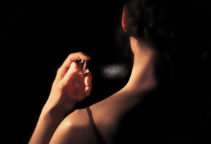 A woman spraying perfume on the nape of her neck in a dimly lit, elegant setting.
