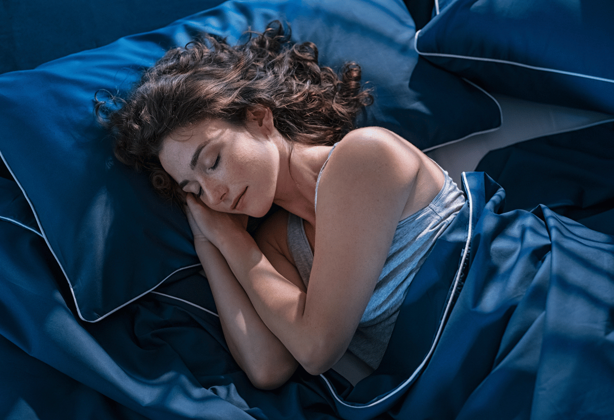A woman peacefully sleeping on a navy blue bed with silky bedding, her hair spread gracefully on the pillow.