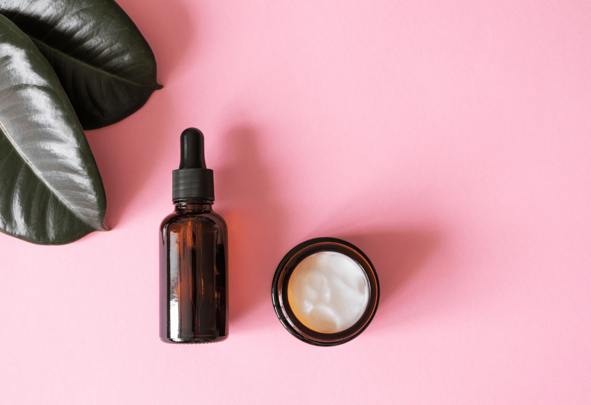 A serum bottle and moisturizer jar on a pink background