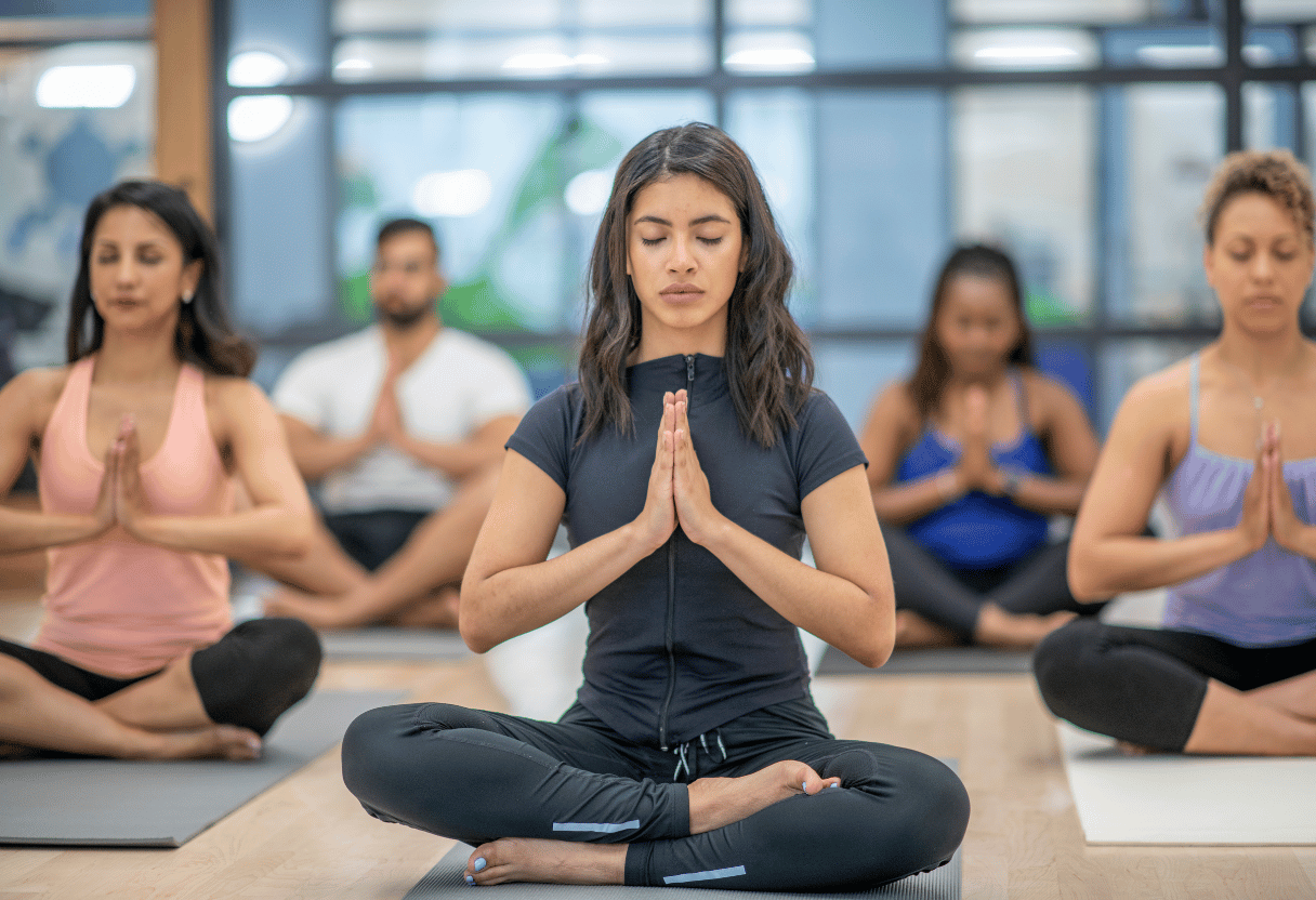 A group of people in a yoga class meditating with their hands in prayer pose, focusing on relaxation in a studio setting.