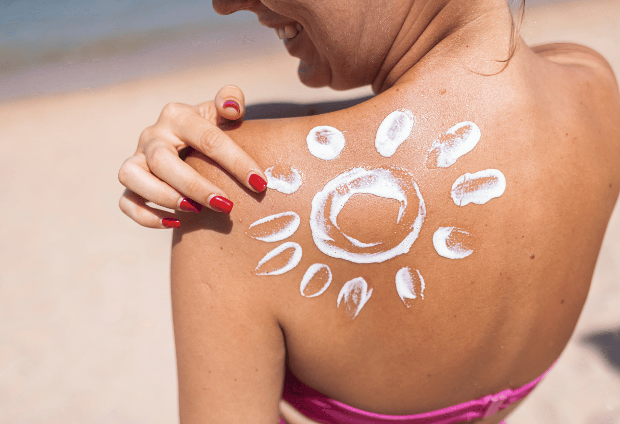 A close-up of a woman’s shoulder with sunscreen lotion applied in the shape of a sun, on a sunny beach.