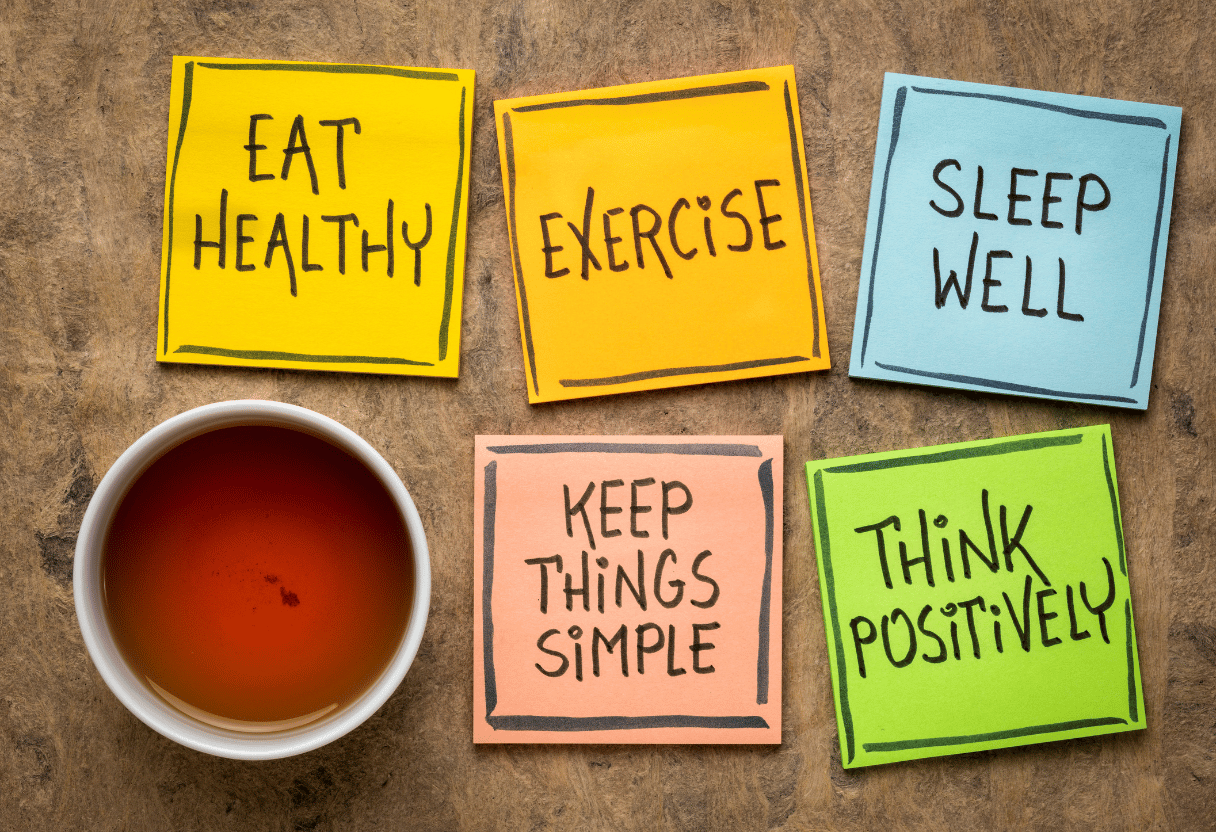 A collection of colorful sticky notes with wellness messages like “Eat Healthy,” “Exercise,” and “Think Positively,” alongside a cup of tea.